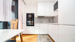 Eine kleine Küche mit weißen Schränken, einem eingebauten Backofen und einem Essbereich mit einem Holzhocker und einem weißen Tisch.