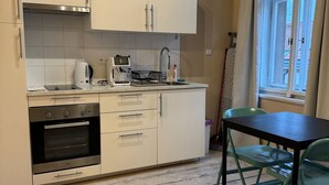 Une cuisine compacte avec des meubles blancs, un four encastré, une machine à café et une fenêtre avec des rideaux.