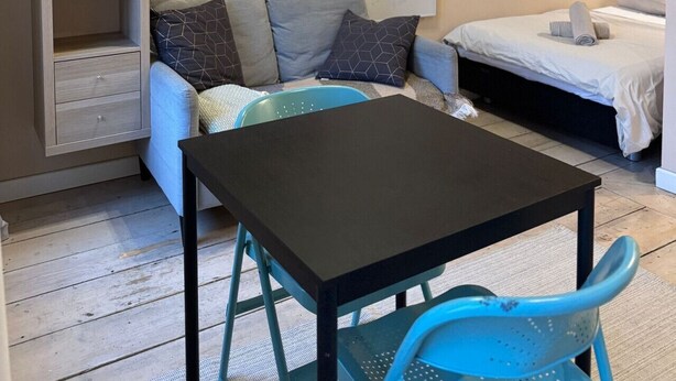 Une pièce de taille modeste comprenant un canapé, un lit, un téléviseur fixé au mur, une petite table et une plante en pot.