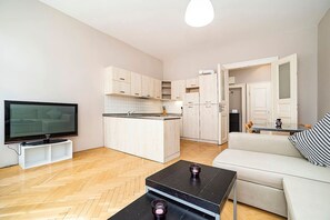 Una sala de estar moderna con un televisor de pantalla plana, un sofá, una mesa de centro y una zona de cocina con armarios y un refrigerador.