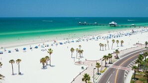 A beach with a pier, palm trees, and a road curving around the beach.