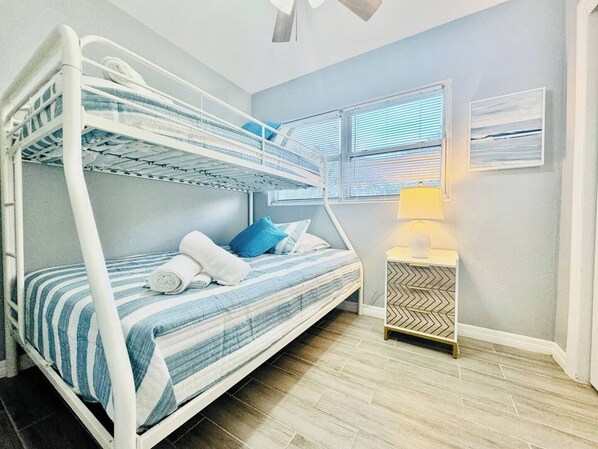 A bunk bed room with a window, a bedside table with a lamp, and a herringbone-patterned cabinet.