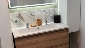 A bathroom with a large mirror, a white sink, wooden drawers, and a green rug on the floor.