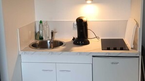 A compact kitchen with white cabinets, a built-in dishwasher, a coffee maker, and a small stove.
