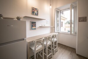 A compact kitchen with a refrigerator, a dining table with chairs, a window with a view, and wall-mounted shelves.