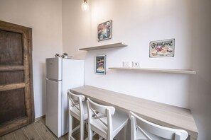A kitchen with a white refrigerator, a wooden door, a light wooden table, and white chairs.