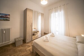 A bedroom with a large mirror, a bed with neatly folded towels, a radiator, and a small trash bin.