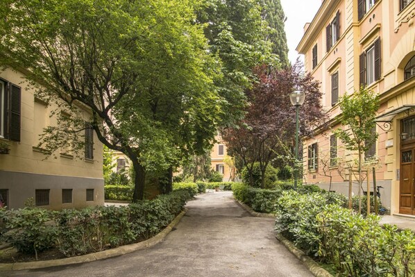 Un estrecho callejón flanqueado por edificios con ventanas y contraventanas, rodeado de exuberante vegetación y un farol.