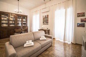 A living room with a sofa, a wooden cabinet with books, a chandelier, and a dining table.