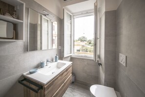 A modern bathroom with a large mirror, a sink, a toilet, and a window.