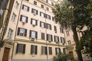 A multi-story building with evenly spaced windows, some with shutters, and a balcony with plants.