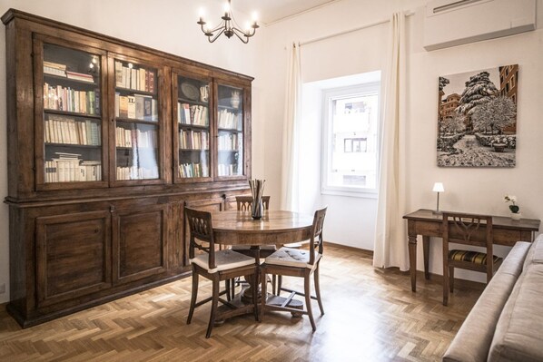 A dining area with a wooden table and chairs, a cabinet with books, and a painting on the wall.