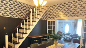 A dining area with a dark wooden table, chairs, and a plant centerpiece. A staircase with a patterned wall leads to another room. - Cane River Living Downtown I Historic District (Natchitoches)