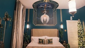 A bedroom with a bed, a wall-mounted artwork, a hanging light fixture, a Christmas tree, and a door. - Cane River Living Downtown I Historic District (Natchitoches)