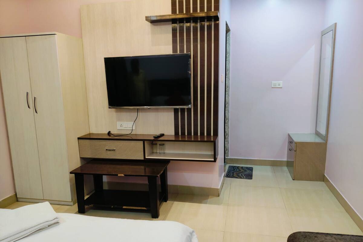 A hotel room with a bed, a desk with a flat-screen TV, a wardrobe, and a small cabinet.