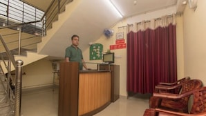 A reception area with a wooden desk, a computer, and a green sign on the wall. - Hotel Jyoti (Siliguri)