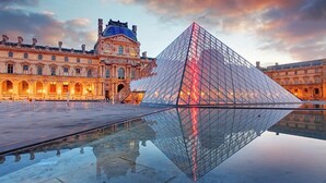 Un'ampia piramide di vetro che si riflette in una piscina, con architettura classica sullo sfondo.