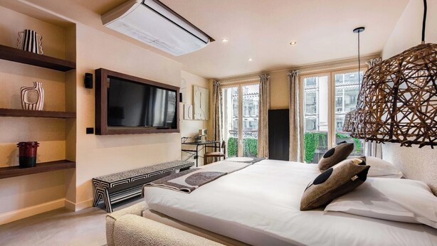 Una camera da letto moderna con un letto grande, una TV a schermo piatto montata a parete, una scrivania con una sedia e un'ampia finestra vista verde.
