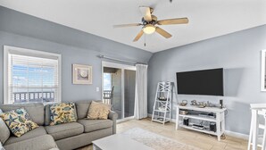 A living room with a grey sofa, a white coffee table, a TV stand, and a ceiling fan. - FFR209 Beach Hideaway by First Flight Rentals (Kill Devil Hills)