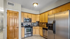 A kitchen with wooden cabinets, stainless steel appliances, and a tiled floor. - FFR209 Beach Hideaway by First Flight Rentals (Kill Devil Hills)