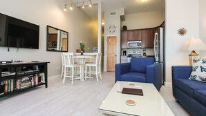 A modern living room with a flat-screen TV, a coffee table, a sofa, and a dining area with a table and chairs. - FFR314 - Just Wright by First Flight Rentals (Kill Devil Hills)