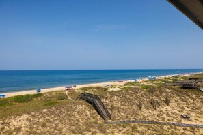 Une plage avec une promenade en bois menant au rivage, des dunes de sable et un ciel bleu dégagé.