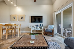 A living room with a TV, two framed pictures, a wicker chair, a sofa, and a dining table with chairs. - FFR315 Seas the Day by First Flight Rentals (Kill Devil Hills)