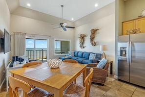 A spacious living area with a dining table, sofa, and kitchen area with a refrigerator. - FFR315 Seas the Day by First Flight Rentals (Kill Devil Hills)