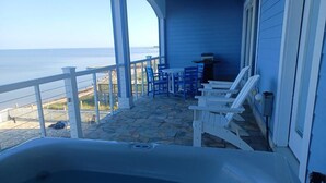 A covered outdoor area with a hot tub, white chairs, and a view of the ocean. - WV25 Surf Shack by First Flight Rentals (Rodanthe)