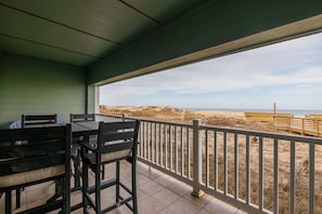 A covered outdoor area with a table and chairs, a view of the beach, and a wooden fence.