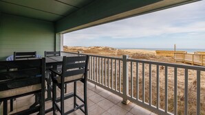 Un'area esterna riparata con tavolo e sedie, vista sulla spiaggia e una recinzione in legno.