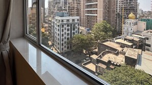 Una ventana con vistas a un paisaje urbano, que incluye varios edificios y un árbol.