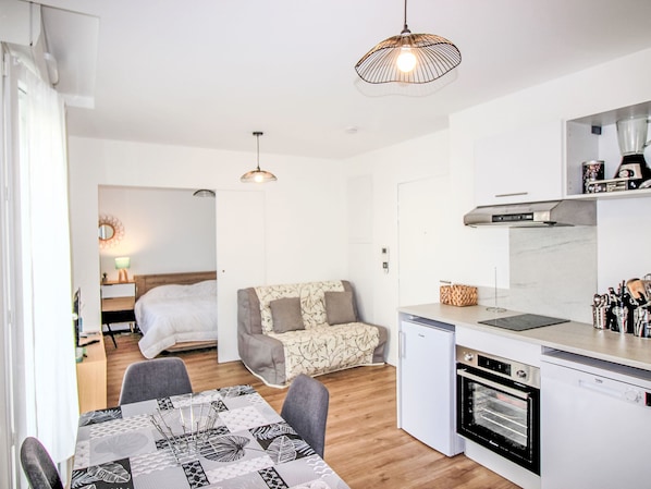 Cozy living area with sofa, dining table, and kitchenette, featuring a separate bedroom with a bed.