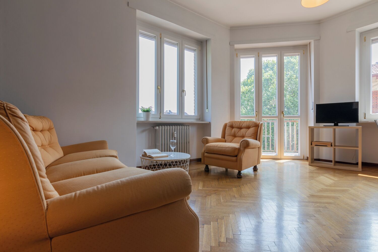 Un salón amplio con un sofá grande, un sillón más pequeño y un televisor sobre un mueble de madera.