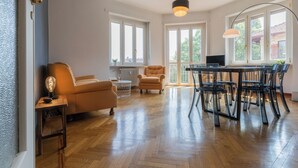 A spacious living room with a wooden herringbone floor, a sofa, a dining table with chairs, and large windows allowing natural light. - Mole View by Wonderful Italy (Turin)