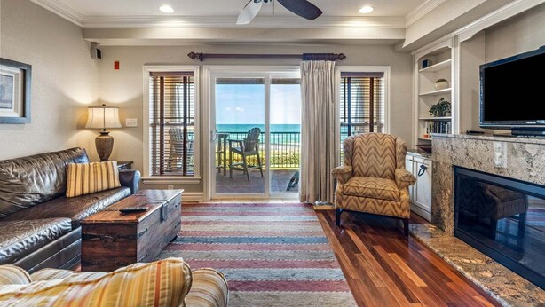 A living room with a sofa, armchair, fireplace, television, and a view of the ocean through large sliding doors. - CSC3M Dawn Patrol by First Flight Rentals (Kill Devil Hills)