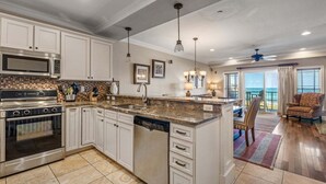 A modern kitchen with a central island, stainless steel appliances, and a view to the living area. - CSC3M Dawn Patrol by First Flight Rentals (Kill Devil Hills)