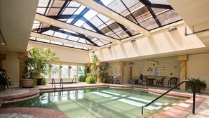 An indoor swimming pool with a glass ceiling, surrounded by potted plants and seating areas. - CSC3M Dawn Patrol by First Flight Rentals (Kill Devil Hills)
