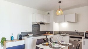 A modern kitchen with white cabinets, a built-in stove, and a dining area with a table set for two. - Cap Océan by Interhome (Capbreton)