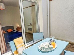 A room with a bed, a table with a tray of cups and a glass of orange juice, and a view of another room through a glass door. - Cap Océan by Interhome (Capbreton)