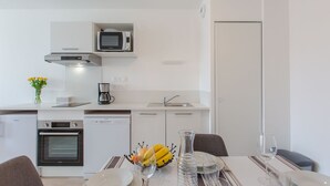 Ett modernt kök med mikrovågsugn, ugn och kaffebryggare. Det finns ett matbord dukat med tallrikar, glas och en fruktskål.