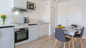 Ett modernt kök med vita skåp, en inbyggd ugn, en mikrovågsugn och en kaffebryggare. Det finns ett matbord med stolar och en vas med blommor på köksbänken.