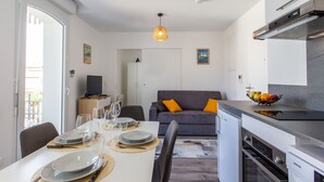 A compact kitchen with a built-in oven, a dining area with a table set for four, and a gray sofa with orange cushions. - Cap Océan by Interhome (Capbreton)