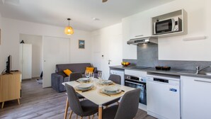 A modern kitchen with a microwave, oven, and dishwasher. There is a dining table with chairs and a sofa in the background. - Cap Océan by Interhome (Capbreton)