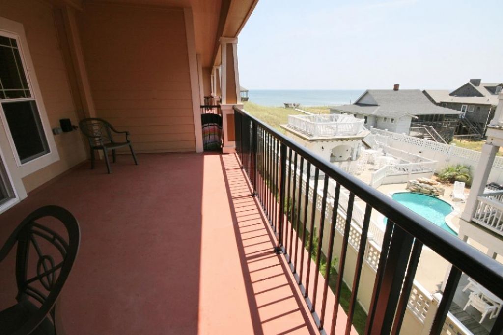 A balcony with a view of the ocean, a pool, and adjacent buildings.
