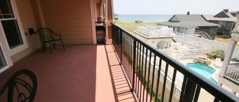 A balcony with a view of the ocean, a pool, and adjacent buildings.