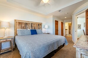 A bedroom with a large bed, a wooden headboard, a nightstand with a lamp, and a dresser. - CSC4E High Roller by First Flight Rentals (Kill Devil Hills)