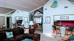A spacious living area with a dark brown sofa, wooden chairs, and a bar area with a red countertop. - SS9 Raynorshine by First Flight Rentals (Kill Devil Hills)