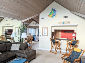A cozy living room with a fireplace, wooden ceiling beams, and a dining area with a red accent wall. - SS9 Raynorshine by First Flight Rentals (Kill Devil Hills)
