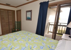 A bedroom with a bed, a chair, a window with curtains, and a view of a balcony.